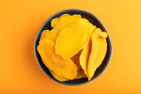 Dried Mango in blue ceramic bowl on orange pastel paper background. Top view, copy space, flat lay.
