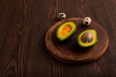 Two Avocado halves with pit and Egg yolk on round wooden cutting board on brown wooden background,