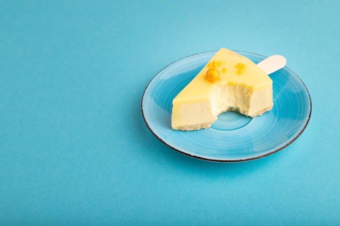 Bitten Yellow Cake pop with sprinkles on blue ceramic plate on blue pastel paper background, side