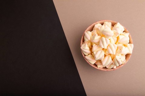 Orange and pink marshmallow in ceramic bowl on black and beige pastel paper background, top view,