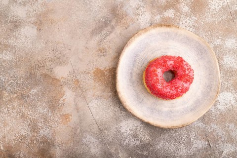 Pink Donut with sprinkles on blue ceramic plate on brown concrete background, top view, flat lay,