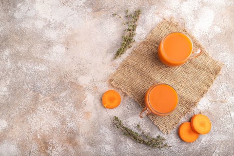 Two glasses with carrot juice, on brown concrete background and linen textile. Diet, healthy eating