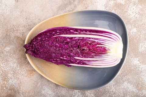 Purple Chinese cabbage on blue plate on brown concrete background, top view, flat lay, close up,