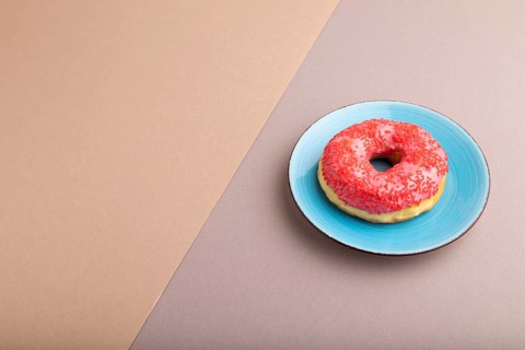 Pink Donut with sprinkles on blue ceramic plate on beige and gray pastel paper background, side