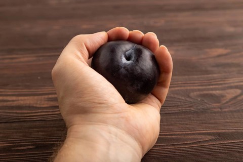 Purple Plum with hand on brown wooden background. Side view, close up. healthy food, vegetable,