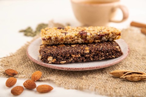 Granola bars with caramel, nuts, flakes in ceramic plate on white wooden background, beige linen