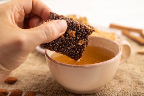 Granola bars with caramel, nuts, flakes in ceramic plate with hand on white wooden background,