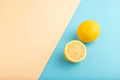 Yellow Lemon Cut in half on orange and blue pastel paper background. Side view, flat lay, copy
