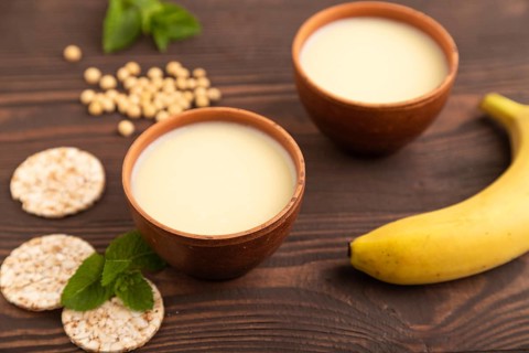 Organic non dairy banana and soy milk in clay cup on brown wooden background. Vegan healthy food
