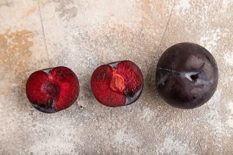Purple Plum Cut in half on brown concrete background. Top view, flat lay, copy space. healthy food,