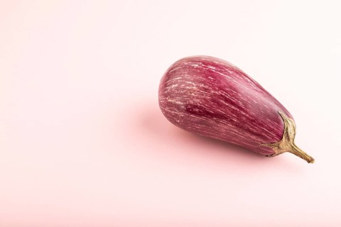 Purple eggplant with white stripes on pink pastel background. Side view, copy space. Tropical,