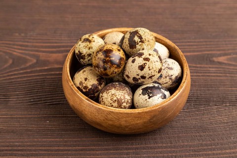 Pile of raw Quail eggs in bowl on a brown wooden background. side view, close up