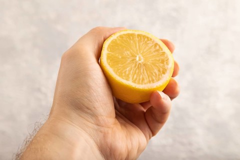 Yellow Lemon Cut in half with hand on gray concrete background. Side view, close up. healthy food,
