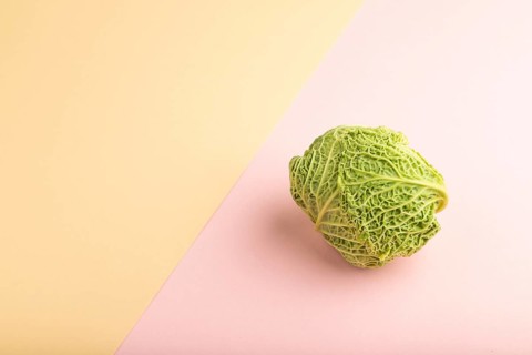 Green lettuce on pink and orange pastel paper background. Side view, copy space. healthy food,