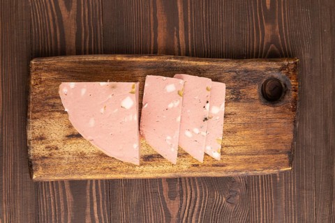 Mortadella sausage on wooden cutting board with pepper and herbs on brown wooden background. Top