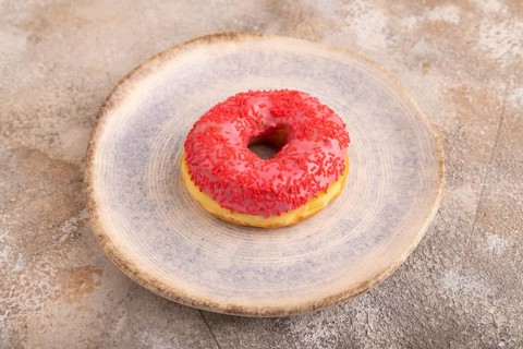 Pink Donut with sprinkles on blue ceramic plate on brown concrete background, side view, close up,