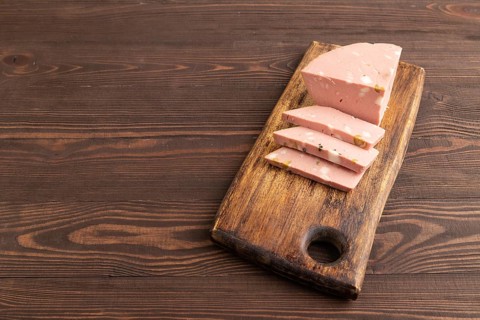 Mortadella sausage on wooden cutting board with pepper and herbs on brown wooden background. Side