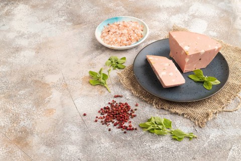 Mortadella sausage on plate with pepper and herbs on brown concrete background and linen textile.