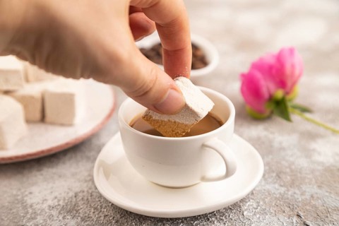 Coffee marshmallow with cup of coffee with hand on brown concrete background. side view, close up,