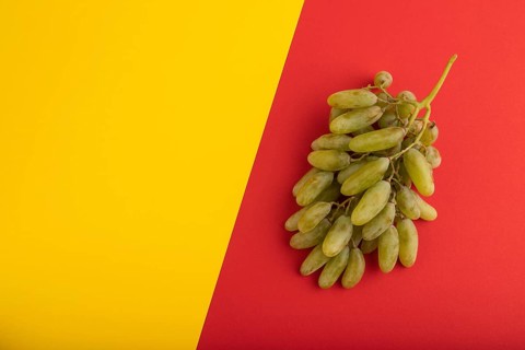 Green grapes on yellow and red paper pastel background. Top view, flat lay, copy space. healthy