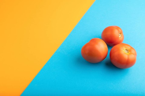 Red tomato on blue and orange pastel paper background. Side view, copy space. healthy food,