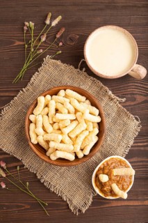 Corn flakes sticks with caramel in wooden bowl on brown wooden background and linen textile. Top