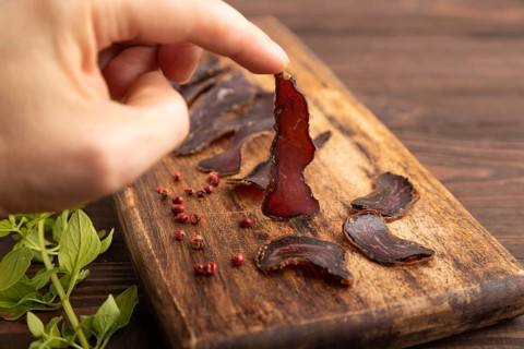 Armenian Basturma dried meat with hand on wooden cutting board with pepper and herbs on brown
