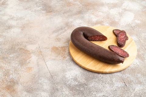 Sujuk sausage on wooden cutting board with pepper and herbs on brown concrete background. Side