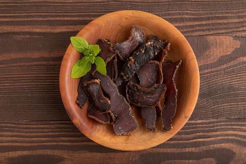 Armenian Basturma dried meat on wooden bowl with pepper and herbs on brown wooden background. Top