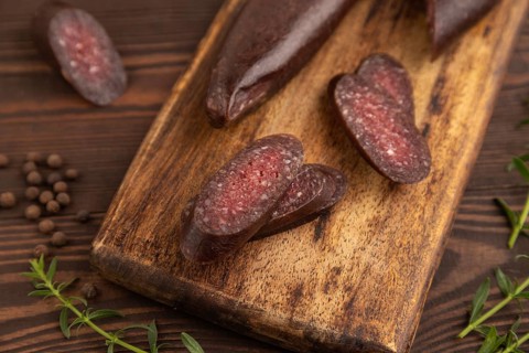 Sujuk sausage on wooden cutting board with pepper and herbs on brown wooden background. Side view,