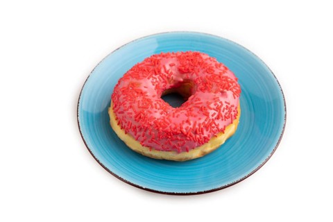 Pink Donut with sprinkles on blue ceramic plate isolated on white background, side view, close up,