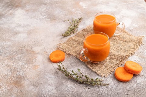 Two glasses with carrot juice, on brown concrete background and linen textile. Diet, healthy eating