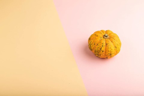 Orange Pumpkin on orange and pink pastel paper background. Side view, copy space. healthy food,
