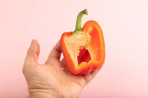 Hand holding sliced Red Cutted pepper on pink pastel background. Side view, copy space. Tropical,