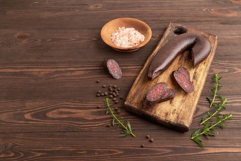 Sujuk sausage on wooden cutting board with pepper and herbs on brown wooden background. Side view,