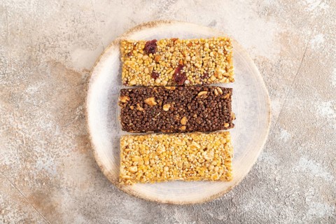 Granola bars with caramel, nuts, flakes in ceramic plate on brown concrete background. Top view,
