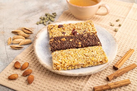 Granola bars with caramel, nuts, flakes in ceramic plate on brown concrete background, beige linen