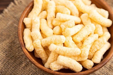 Corn flakes sticks with caramel in wooden bowl on brown wooden background and linen textile. Side