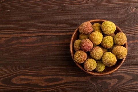 Ripe Lychee on clay bowl on brown wooden background, top view, flat lay, copy space, minimalism
