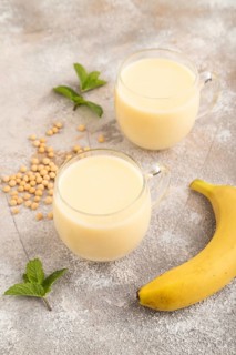 Organic non dairy banana and soy milk in glass on brown concrete background. Vegan healthy food