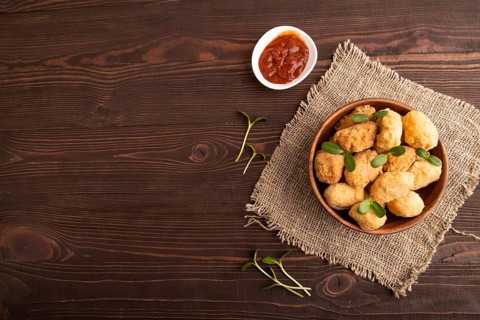 Fried crispy Chicken Nuggets with ketchup, microgreen on brown wooden background and linen textile.