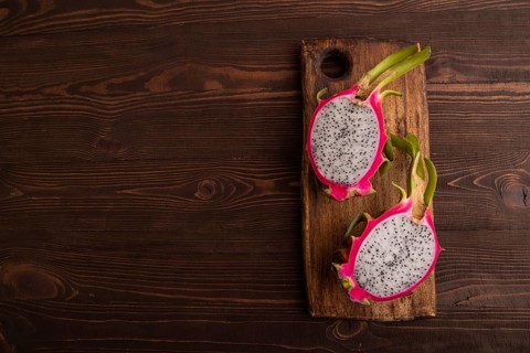 Ripe Pitaya on cutting board on brown wooden background, top view, flat lay, copy space, minimalism
