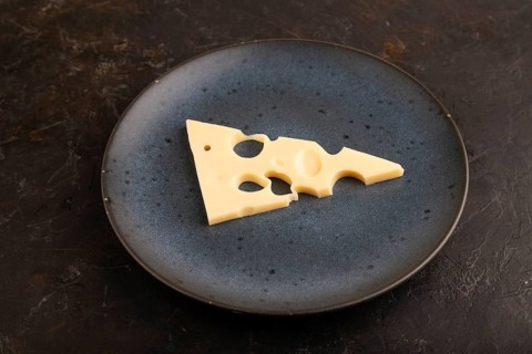 Piece of cheese with holes on blue plate on black concrete background, side view, close up,