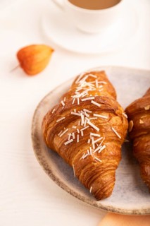 Croissant on blue plate on white wooden background and orange linen textile, cup of coffee, side