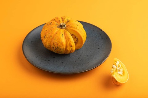 Orange Pumpkin cutted on blue plate on orange pastel paper background. Side view, copy space,