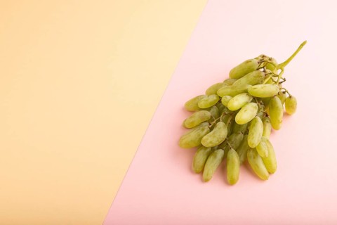 Green grapes on orange and pink paper pastel background. Side view, copy space. healthy food,