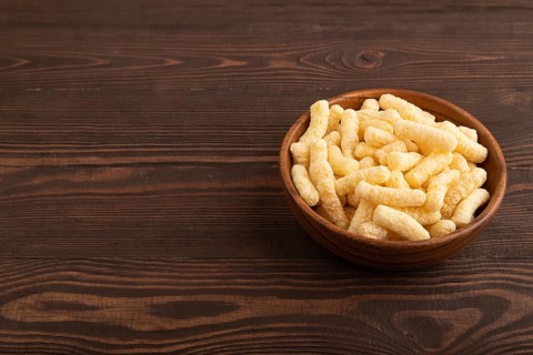 Corn flakes sticks with caramel in wooden bowl on brown wooden background. side view, copy space