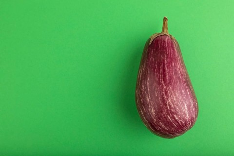Purple eggplant with white stripes on green pastel background. Top view, flat lay, copy space.