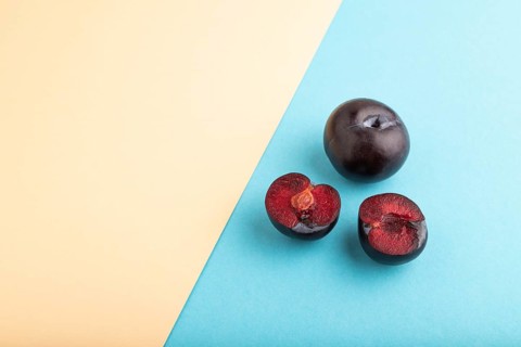 Purple Plum Cut in half on orange and blue pastel paper background. Side view, copy space. healthy