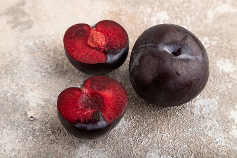 Purple Plum Cut in half on brown concrete background. Side view, close up. healthy food, vegetable,